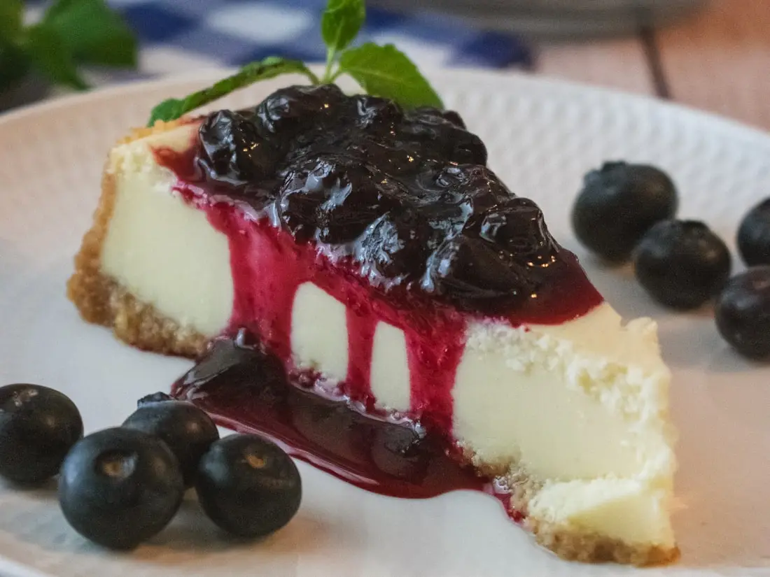 Stück Cheesecake mit Blaubeersauce auf einem weißen Teller