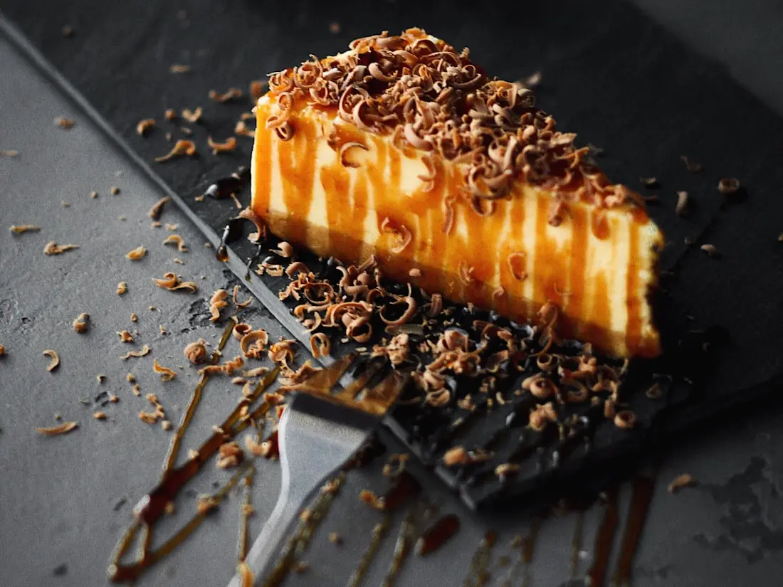 Cheesecake-Riegel mit Karamell und Schokoladenraspeln auf einem dunklen Teller