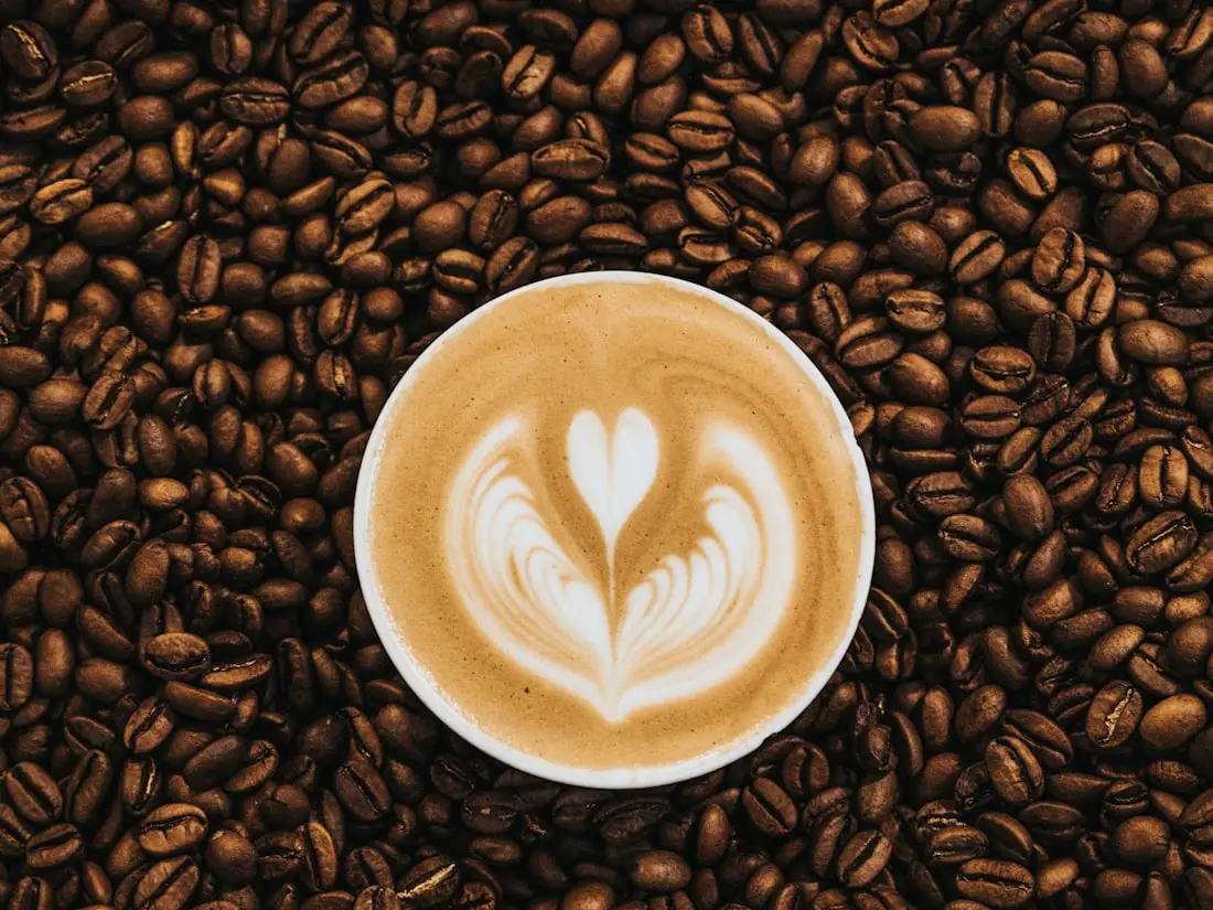 Tasse Cappuccino mit Latte Art, umgeben von Kaffeebohnen