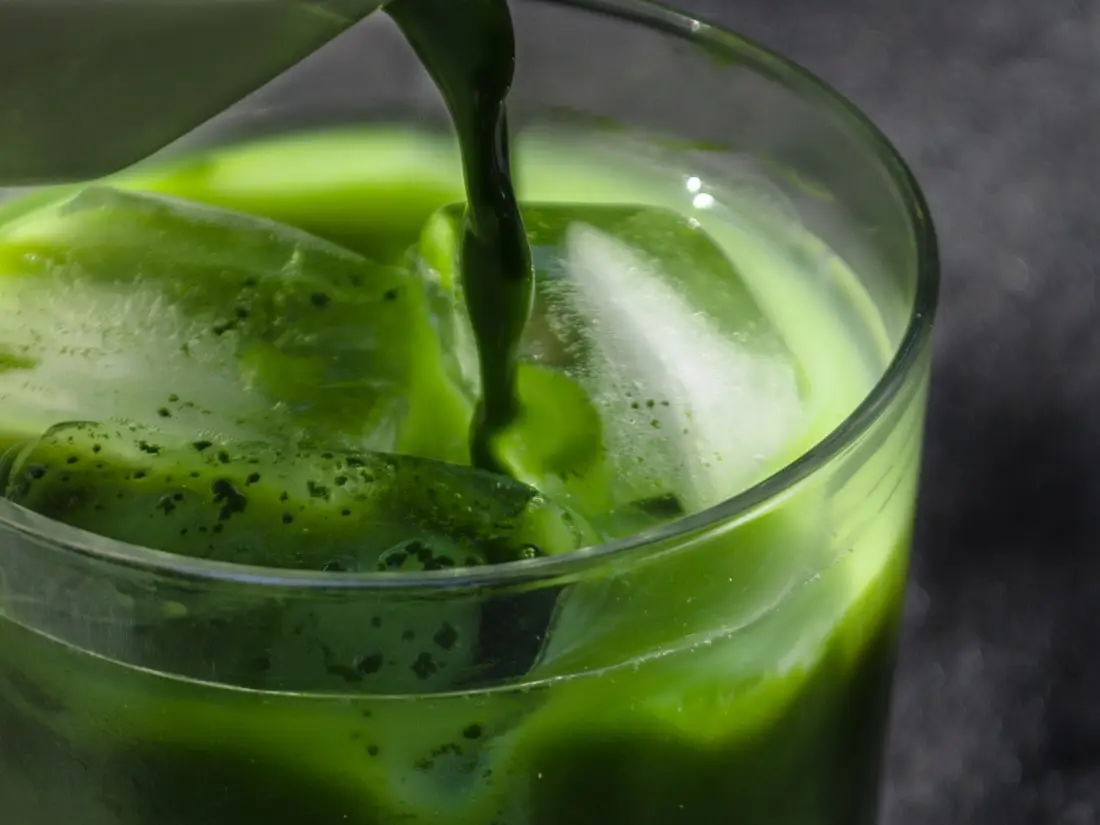 Matcha wird aus einem Krug über Eiswürfel in ein Glas gegossen